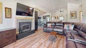 A living room with a fireplace, leather sofa, and a television. - Riverfront house w/ valley & distant mountain views, fireplace, w/d, wifi (Stowe)