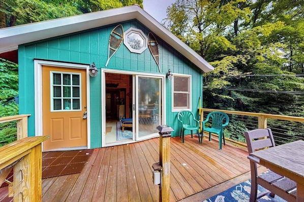 Une maison turquoise avec une terrasse en bois, une porte-fenêtre coulissante et un petit espace salon extérieur.