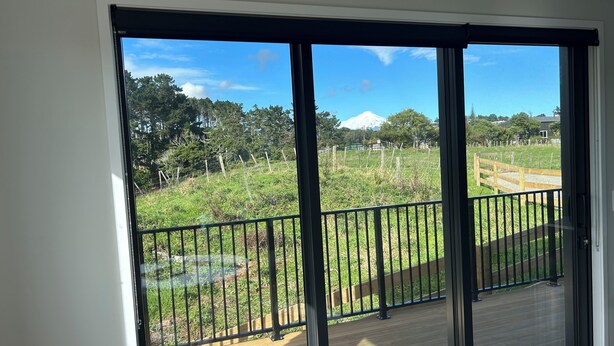 Un balcon donnant sur un champ verdoyant, une terrasse en bois et une montagne à l’horizon.