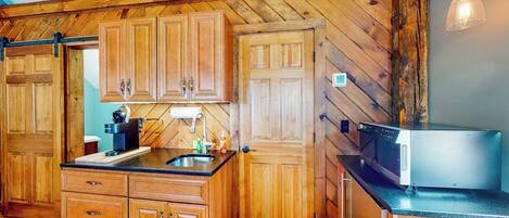 Una cocina con armarios de madera, encimera negra y microondas.