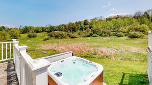 Ett bubbelbad på en terrass med utsikt över en gräsklädd äng och träd.