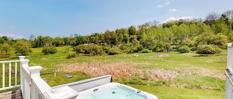 Een bubbelbad op een terras met uitzicht op een grasveld en bomen.