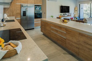 Eine moderne Küche mit einem Edelstahl-Kühlschrank, Holzschränken, einem eingebauten Ofen und einer großen Kochinsel mit einer Blumenvase.
