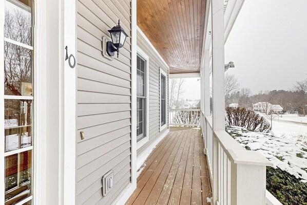 A covered porch with a wooden floor, a wall-mounted lantern, and a view of a snowy landscape.