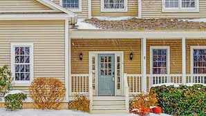 A two-story house with a front porch, a blue door, and a snow-covered roof. - Cozy home near park, deck, patio, bbq, soaking tub, TV, basketball, office, w/d (South Burlington)