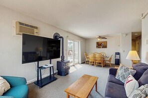 A living room with a flat-screen TV, a wood-burning stove, a sofa, a coffee table, and a dining area with chairs.