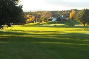 A golf course with a clubhouse, trees, and a clear sky.