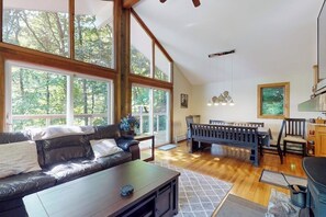 Ein geräumiges Wohnzimmer mit großem Fenster, einem dunkelbraunen Ledersofa, einem Holztisch und einem Billardtisch.