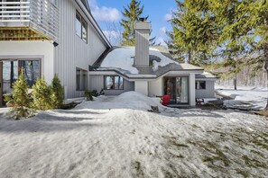 Ein modernes Haus mit schneebedecktem Dach, Schornstein und einer kleinen Veranda.