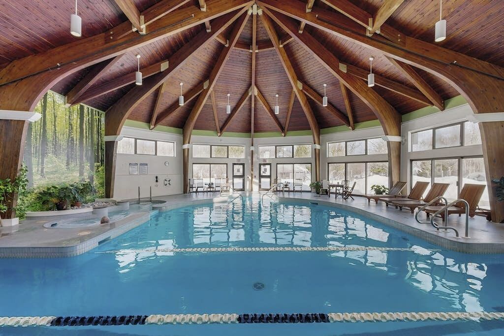 Ein Hallenbad mit hoher Holzbalkendecke, großen Fenstern und Liegestühlen.