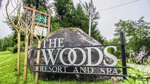 A large rock with 'The Woods Resort and Spa' written on it, surrounded by greenery. - Recently updated home with shared hot tub, pool, and easy ski access (Killington)