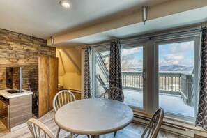 A dining area with a round table, chairs, a stone wall, and a view through large glass doors. - Newly remodeled ski condo near bus to slopes with free WiFi & full kitchen (Killington)