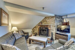 A cozy living room with a stone fireplace, a flat-screen TV, and a comfortable sofa set. - Newly remodeled ski condo near bus to slopes with free WiFi & full kitchen (Killington)