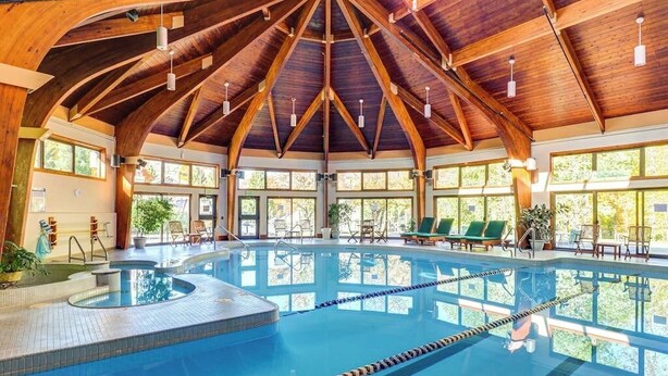 En stor indendørs swimmingpool med træloft og flere vinduer.