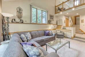 A living room with a sofa, a glass coffee table, a lamp, a dreamcatcher, and a staircase. - Resort townhome with on-site pool, hot tub & easy ski access (Killington)