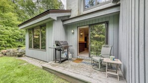 Et moderne hus med en terrasse, grill og spiseplads med stole og bord.