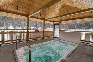 A wooden cabin with a hot tub, wooden deck, and a view of a snowy forest. - Ski-In/ski-out condo with views, pool, hot tubs, gym & tennis access (Killington)