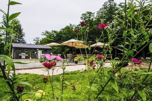 Un jardín con mobiliario exterior, sombrillas, un edificio pequeño y diversas plantas.