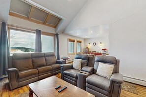 A living room with a sofa set, a coffee table, and a dining area in the background. - Ski-In/ski-out condo with views, pool, hot tubs, gym & tennis access (Killington)