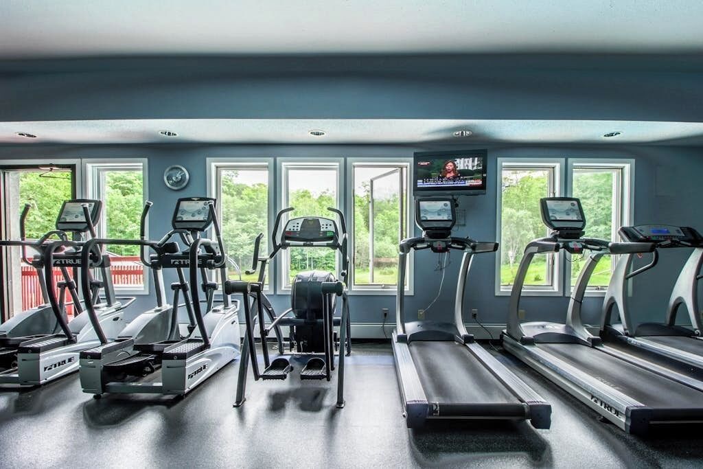 Une salle de sport équipée de tapis de course, de vélos elliptiques et d’un écran de télévision.