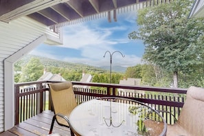 Ein Balkon mit rundem Glastisch, zwei Stühlen und Blick auf eine grüne Landschaft.