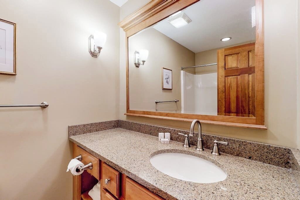 Une salle de bain avec un lavabo à vasque en granit, un grand miroir et une porte en bois.