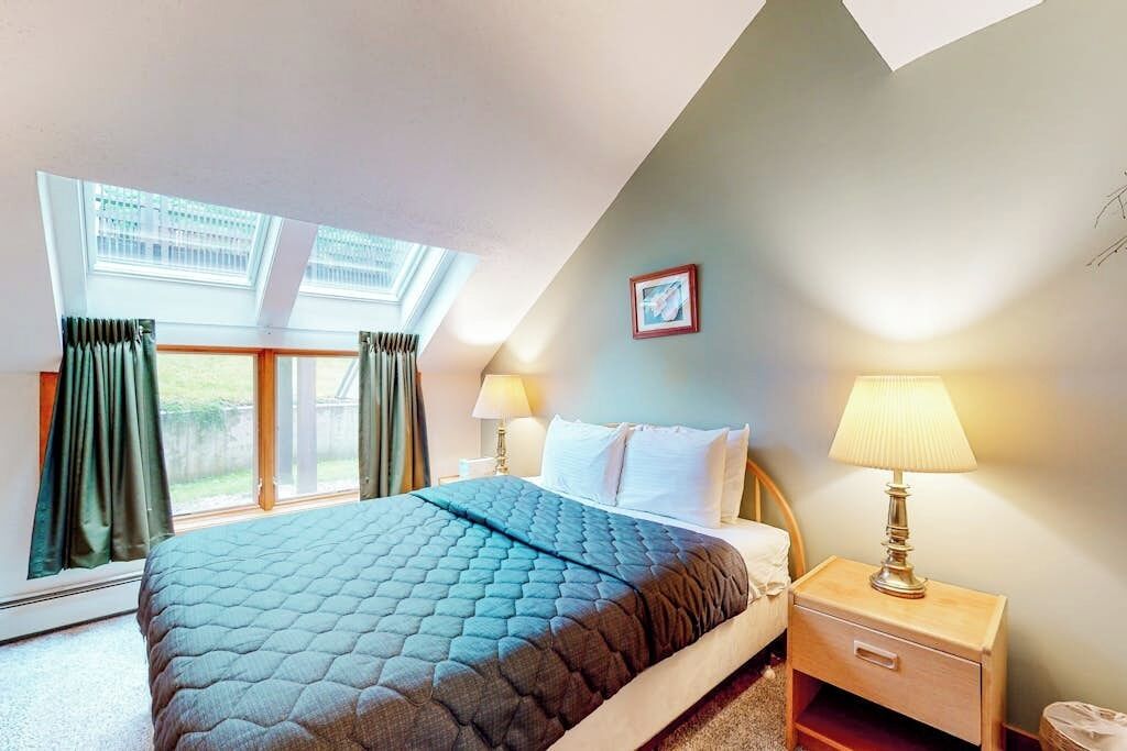 A bedroom with a bed, two bedside lamps, a nightstand, a window with curtains, and a framed picture on the wall.