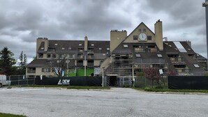 Ein mehrstöckiges Gebäude mit einem Uhrturm, Baugerüsten und einer grünen Baustellenabsperrung.