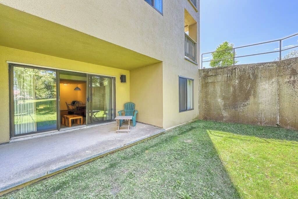 A modern building with a yellow exterior, large sliding glass doors leading to a covered patio area with a small table and chairs.