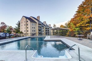 A swimming pool with a hot tub, surrounded by a building with balconies and a fenced area with trees. - Welcoming condo near the slopes with free WiFi and full kitchen (Killington)