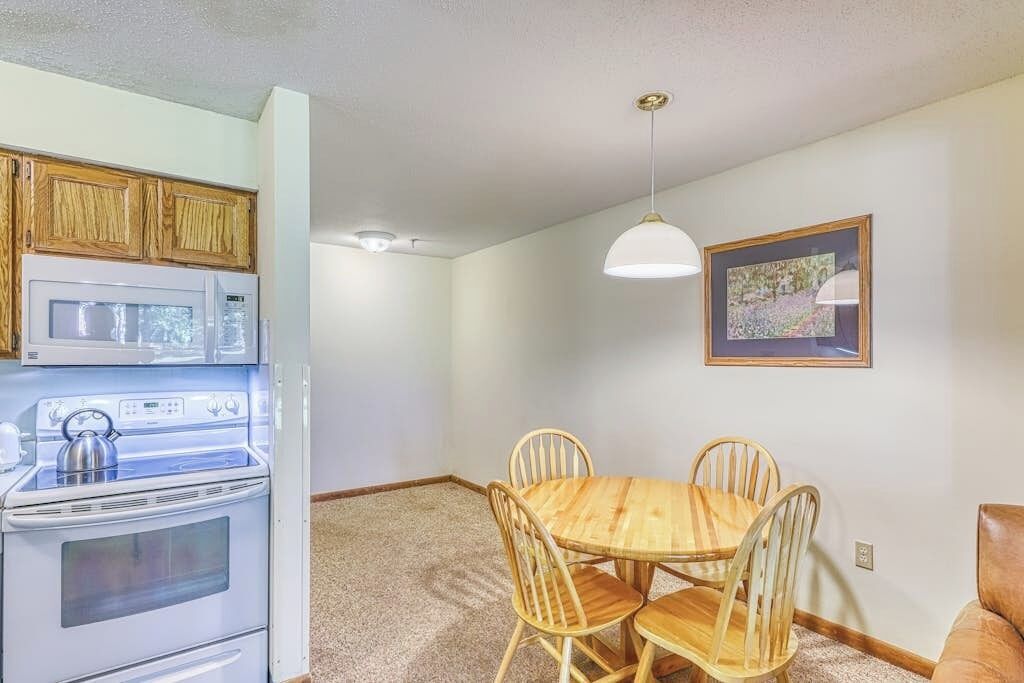 A kitchen with wooden cabinets, a white stove, and a dining table with four chairs.