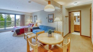 Une pièce comprenant un lit, un canapé bleu, une table à manger avec des chaises, un luminaire au plafond et une vue par la fenêtre.