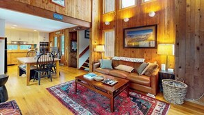 A wooden interior with a dining area, a sofa, and a staircase. - Ski home in the woods with a private hot tub & mountain views (Fayston)