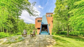 A modern building with a unique architectural design, surrounded by lush greenery. - Ski home in the woods with a private hot tub & mountain views (Fayston)