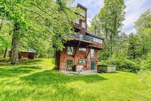 A multi-story wooden cabin with a balcony, surrounded by lush greenery. - Ski home in the woods with a private hot tub & mountain views (Fayston)