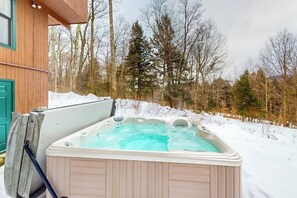 A hot tub in a snowy outdoor setting with a wooden cabin in the background. - Ski home in the woods with a private hot tub & mountain views (Fayston)