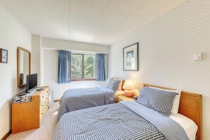 Ein Schlafzimmer mit zwei Betten, einem Schminktisch, einem Fernseher, einem Fenster mit Vorhängen und einer Lampe.