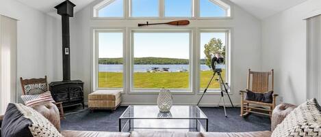 A living room with a large window, a fireplace, a tripod, and a rocking chair.