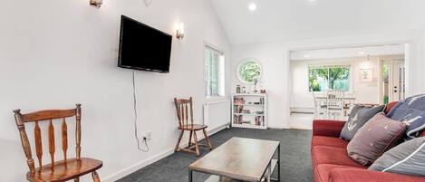 A living room with a TV, two wooden chairs, a red sofa, and a coffee table.