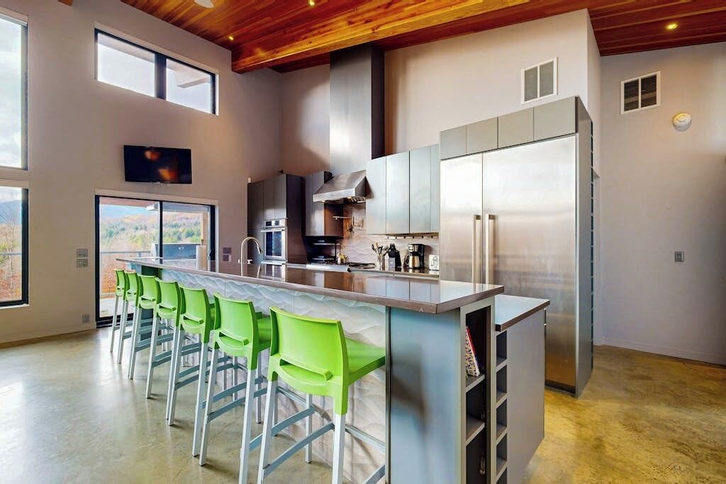A modern kitchen with a central island, bar stools, and a large refrigerator.