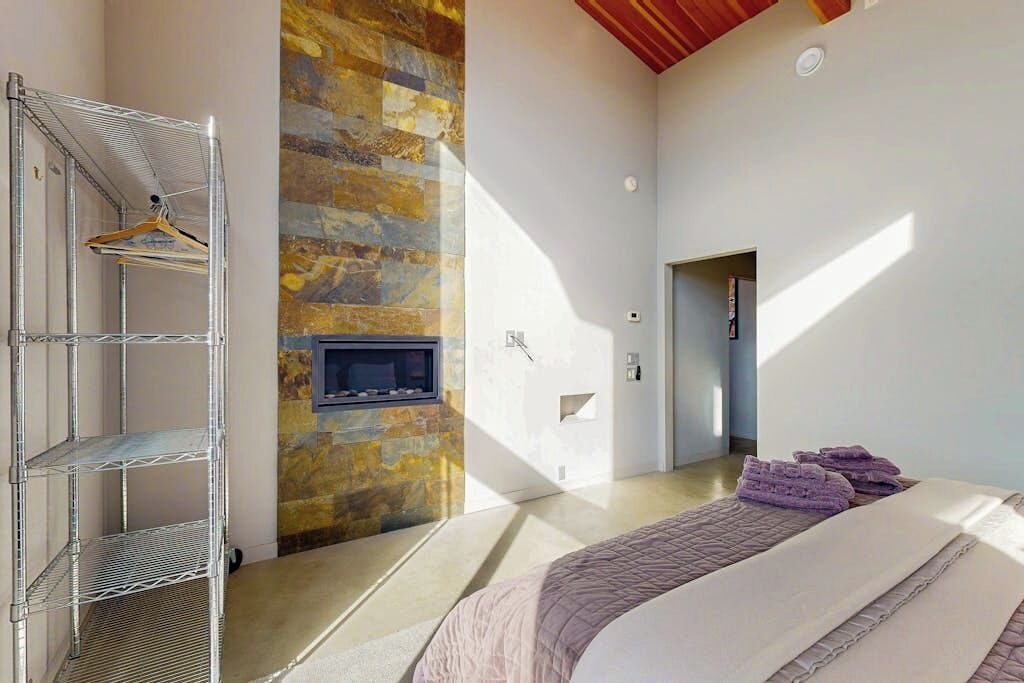 Une chambre à coucher avec un lit, un téléviseur fixé au mur en pierre, une étagère en métal et une porte donnant sur une autre pièce.
