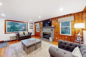 Ein Wohnzimmer mit Kamin, großen Fenstern, einer Couch und einem Couchtisch.