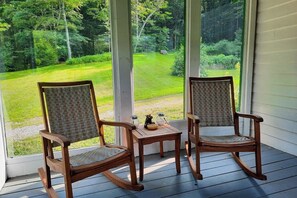 Eine Veranda mit zwei Schaukelstühlen und einem kleinen Tisch, mit Blick auf eine grüne Landschaft.