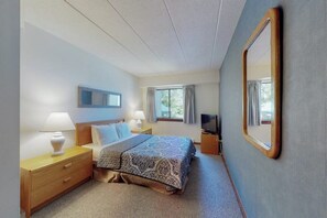 Een hotelkamer met een bed, nachtlampjes, een televisie, een raam met gordijnen en een spiegel.
