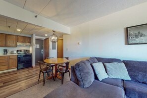 A modern kitchen with wooden cabinets, a dining table with chairs, and a gray sofa with patterned cushions. - Mountain view condo with full kitchen and free WiFi (Killington)