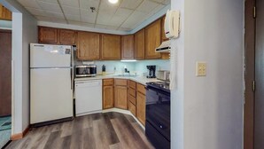 Una cocina con gabinetes de madera, un refrigerador, un microondas, un lavavajillas y una estufa.