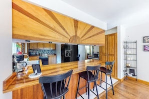 Eine moderne Küche mit Holzboden, einer zentralen Kochinsel mit Barhocker und einem eingebauten Backofen.