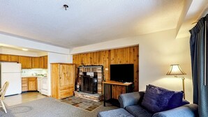 Una sala de estar con chimenea, un sofá, un televisor y una cocina al fondo.