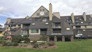 Un edificio de varios pisos con un reloj en la fachada, balcones y un pequeño jardín.