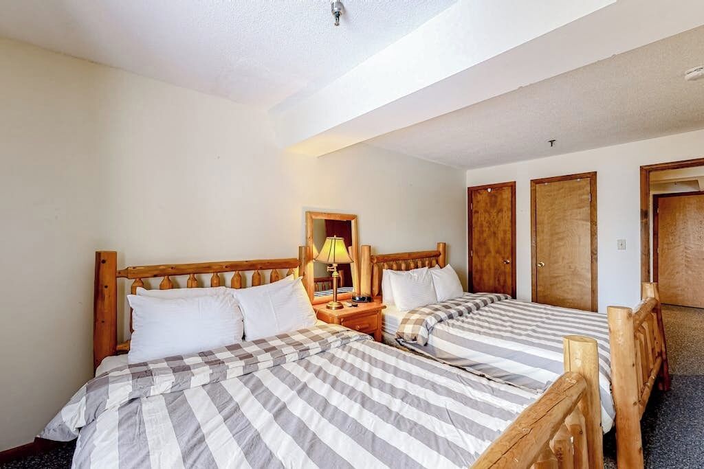 A hotel room with two beds, wooden headboards, a nightstand, a mirror, and a door.